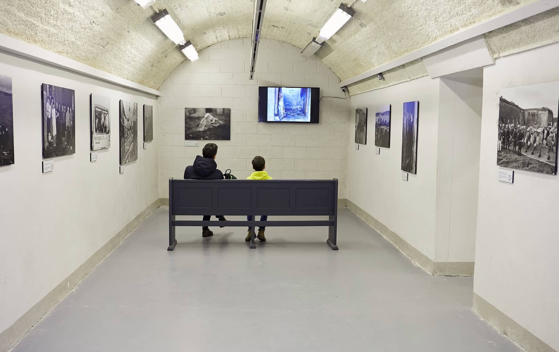 Two visitors watching historic prison footage in an exhibition room at Spike Island.