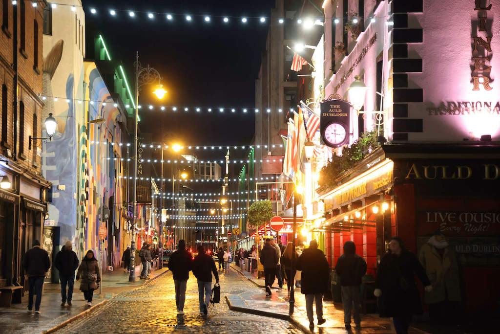 People walking under strings of lights along a lively Temple Bar street at night.