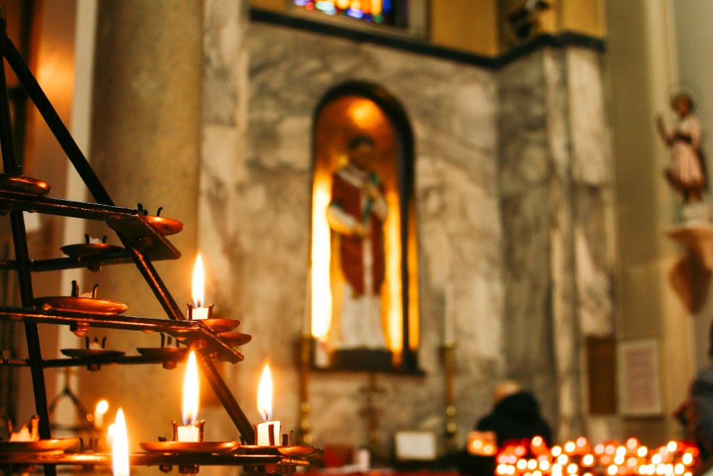Lit candles inside a Whitefriar Street Church, Dublin, with a St Valentine statue in the background.