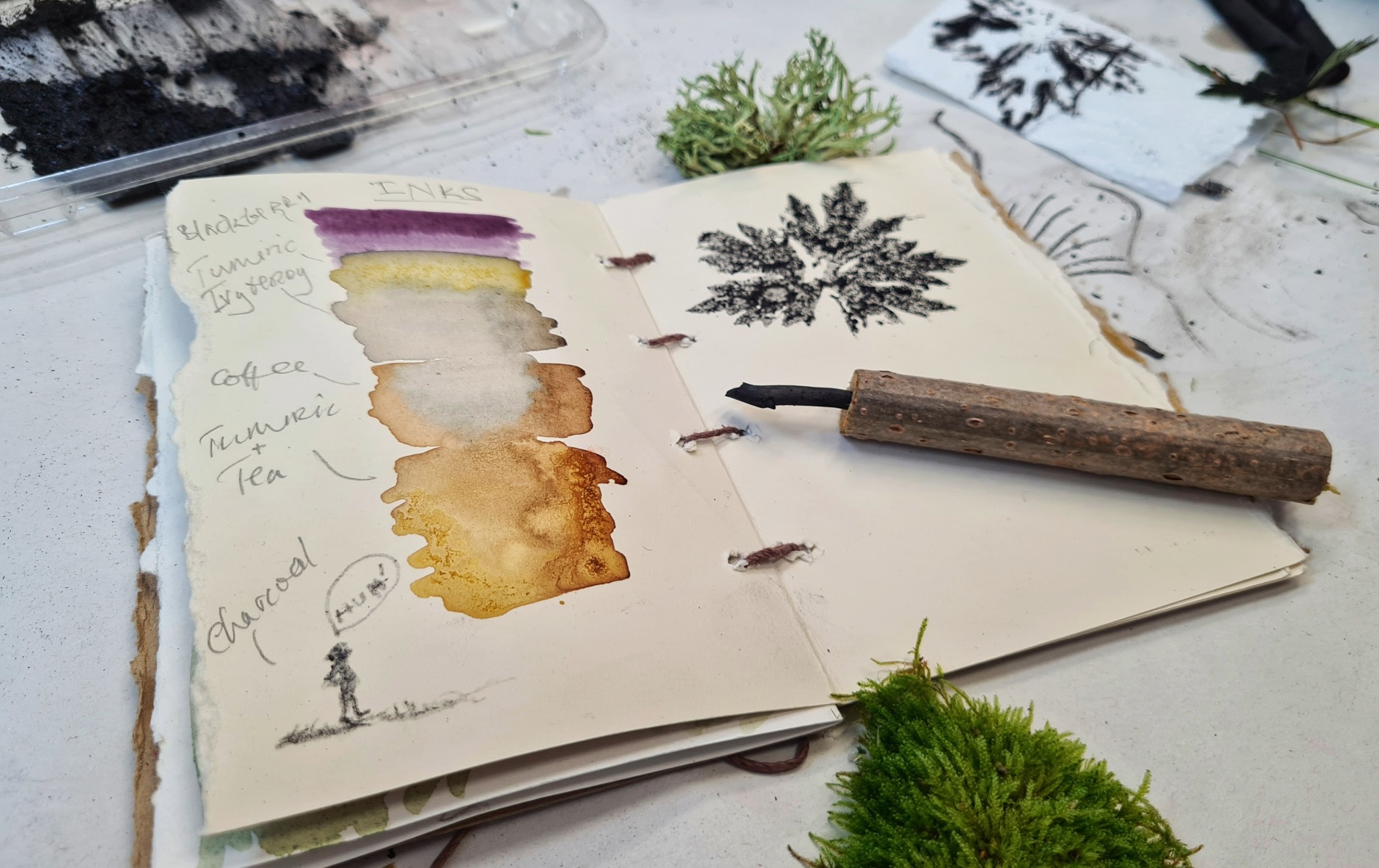 Handmade sketchbook showing natural inks and a leaf print with a rustic tool.