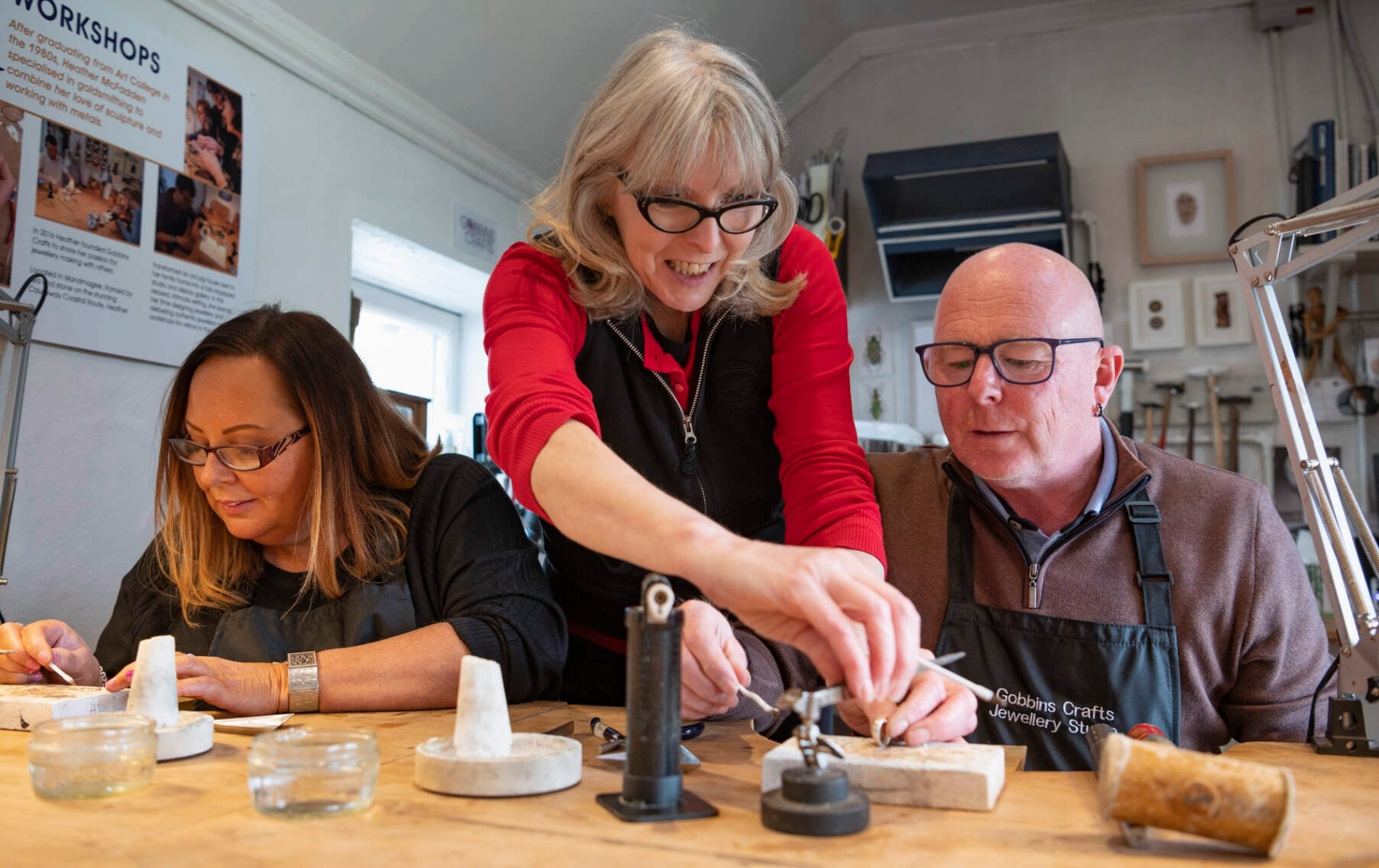 Woman teaching jewellery making to two people in a workshop in Ireland.