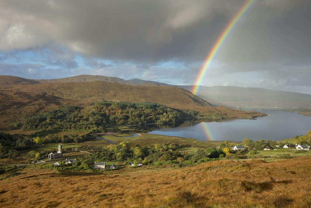 Rainbow arching over hills, a lake and scattered cottages in the scenic Dunlewey countryside, County Donegal.