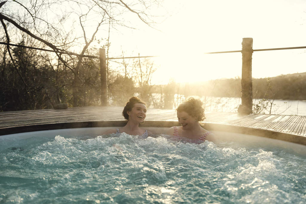 Two women enjoying an outdoor hot tub at sunset, with steam rising and woodland backdrop at Finn Lough, Fermanagh.