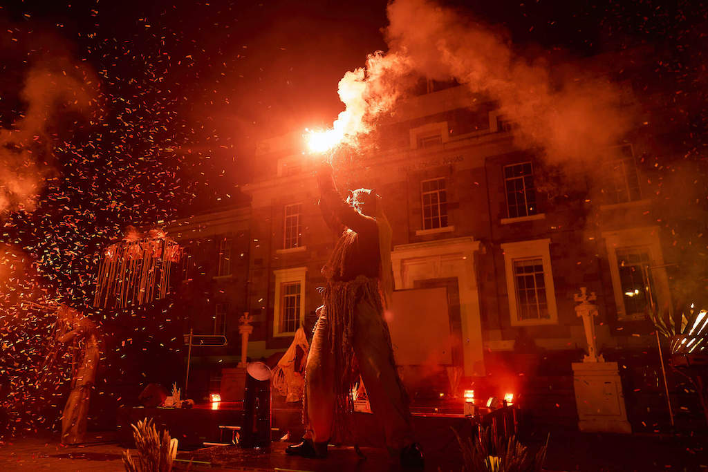 Performer on stage at night with red flare during Kerry's Halloween celebrations.