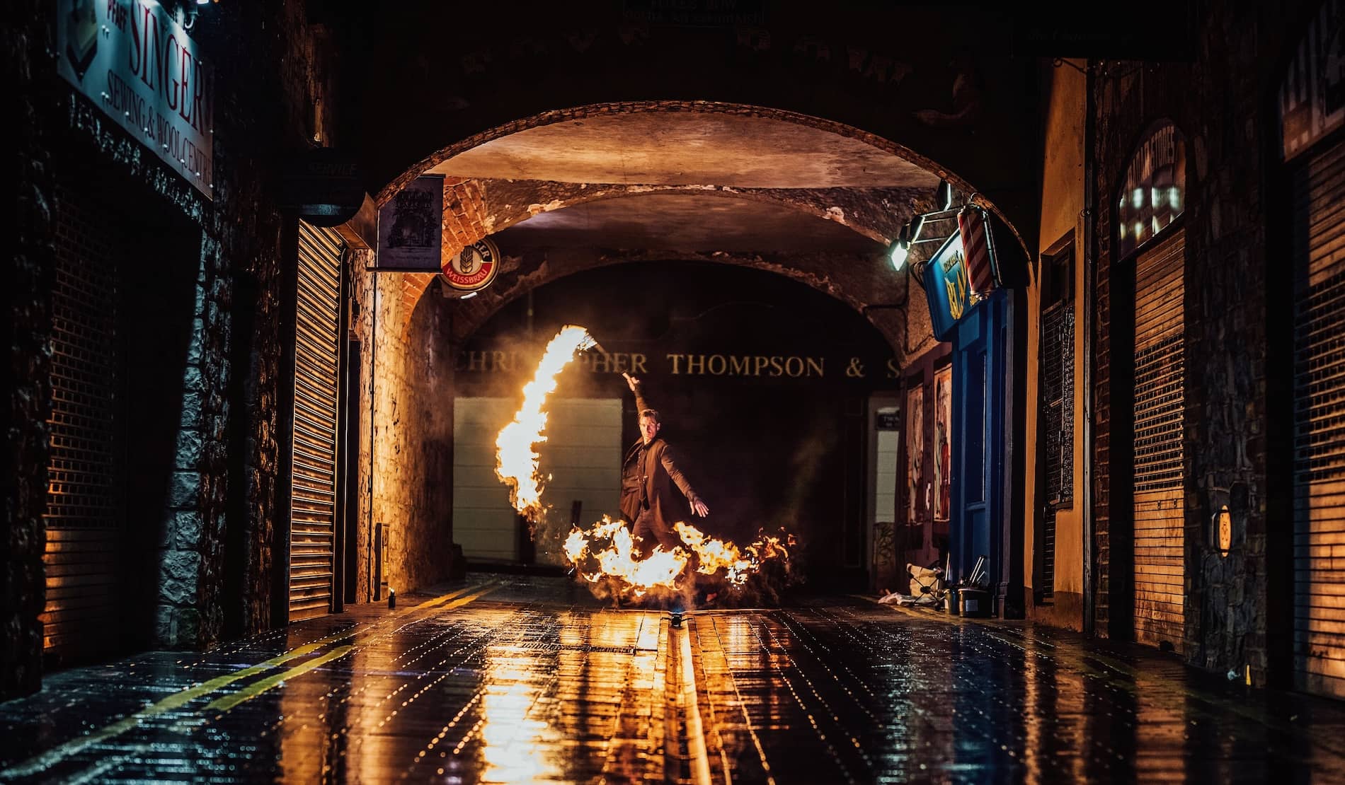 Fire performer spins flaming props in an arched alleyway at night, with wet cobblestones reflecting the glow in Limerick.
