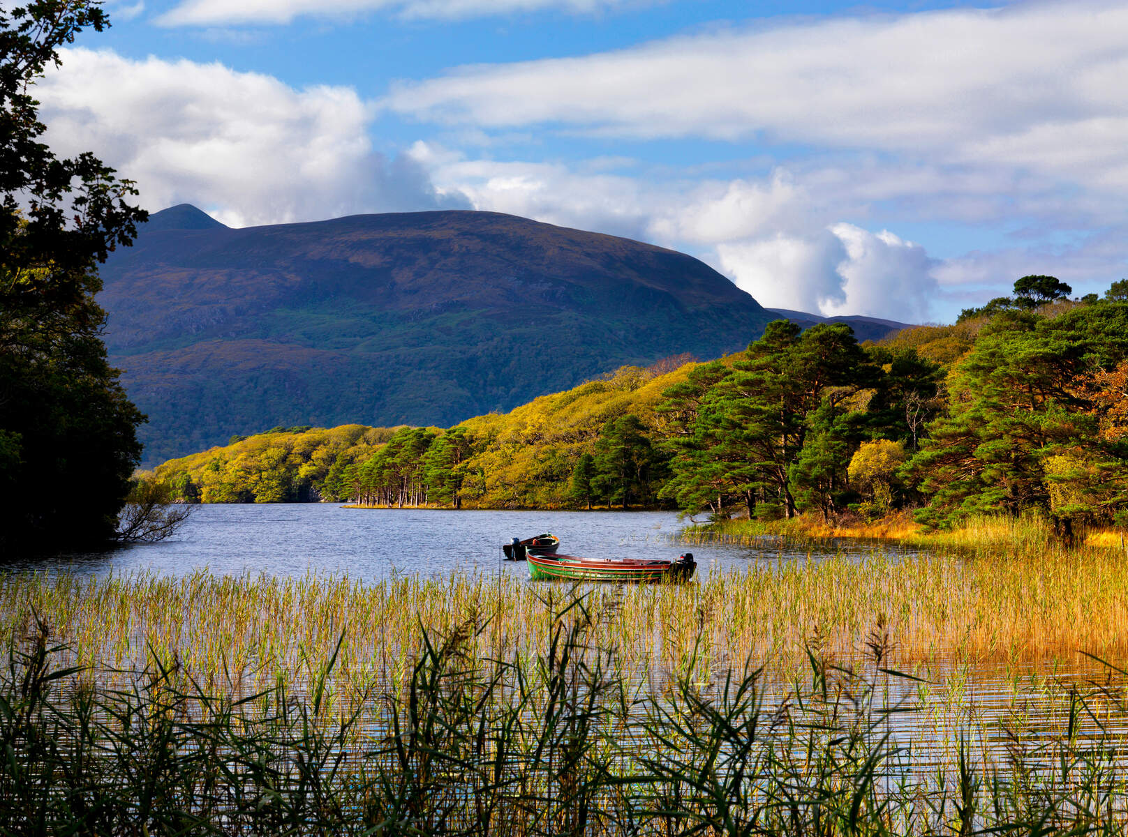 Boats rest on a lake surrounded by autumn trees with mountains rising in the background in Killarney National Park, Kerry.