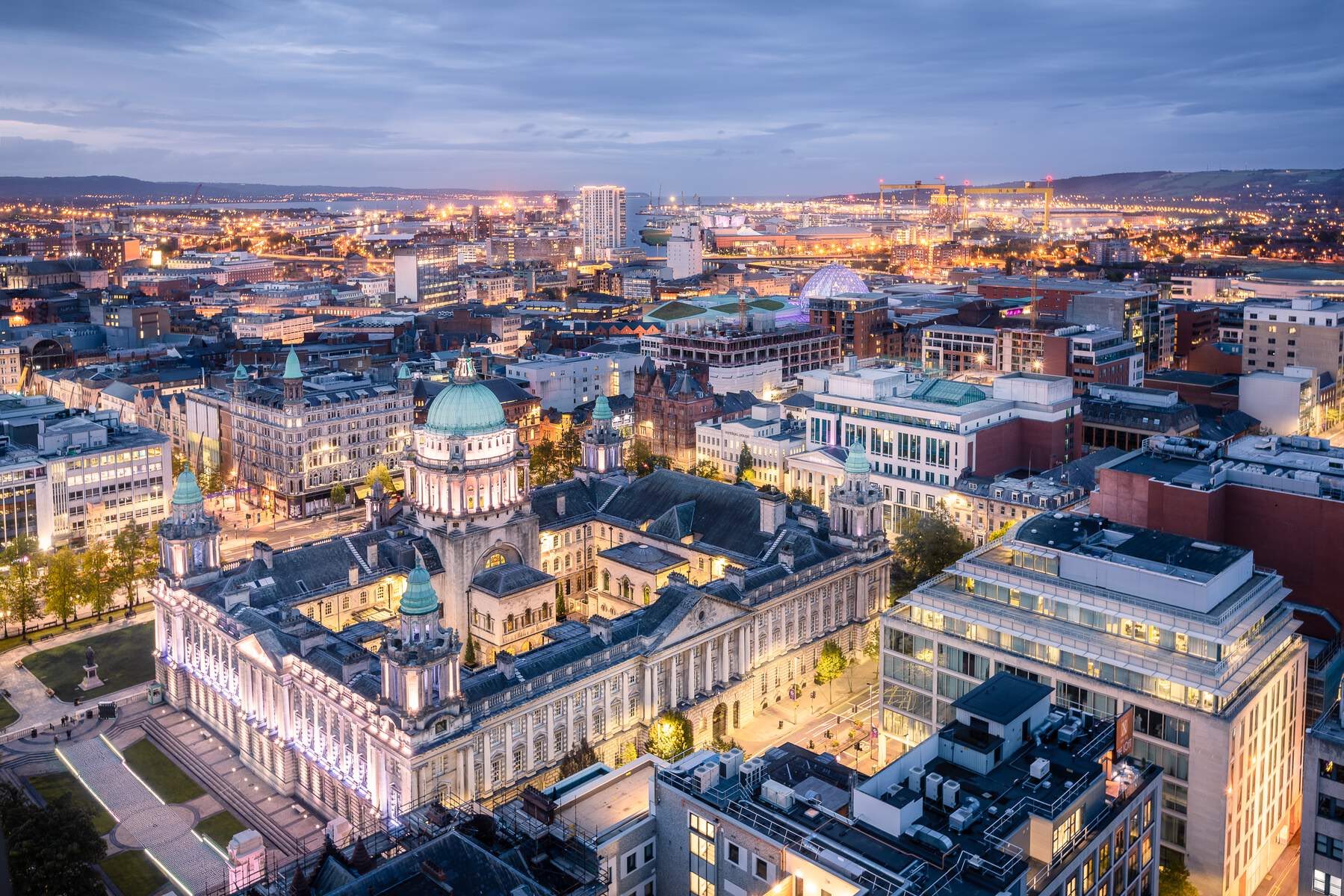 Aerial view of Belfast city at dusk with City Hall lit up.