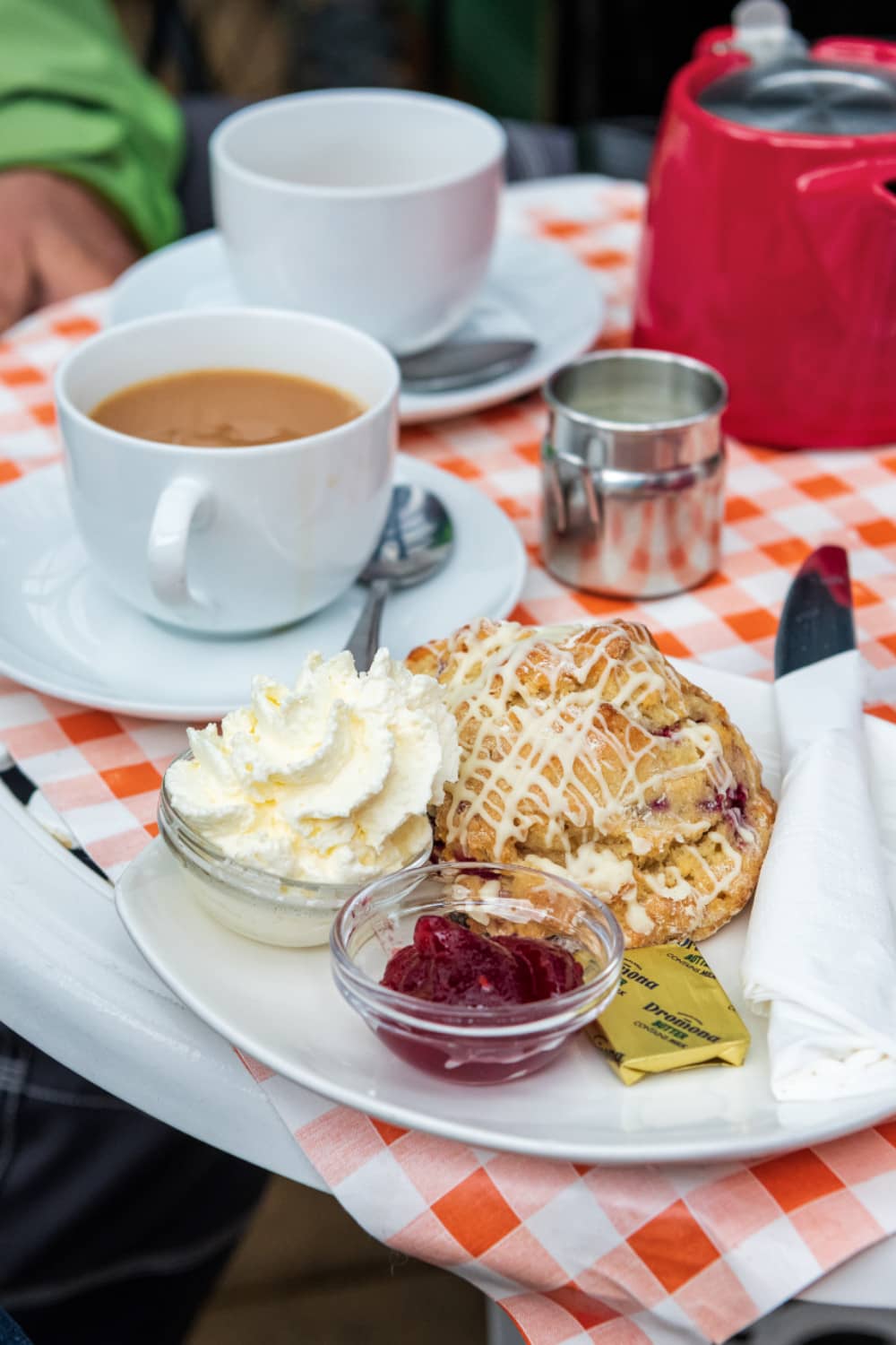 Tea with a fruit scone, cream, and jam served on a checkered tablecloth in Derry~Londonderry.