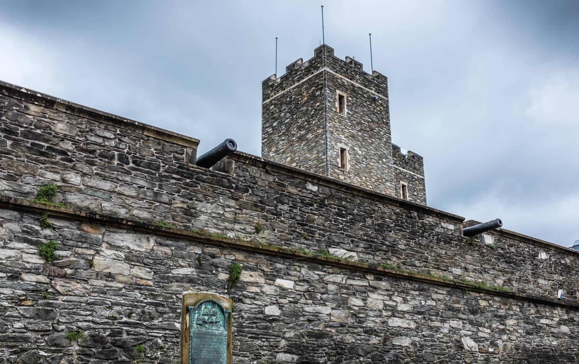 Stone walls and tower of Derry~Londonderry with cannons on display against a cloudy sky.