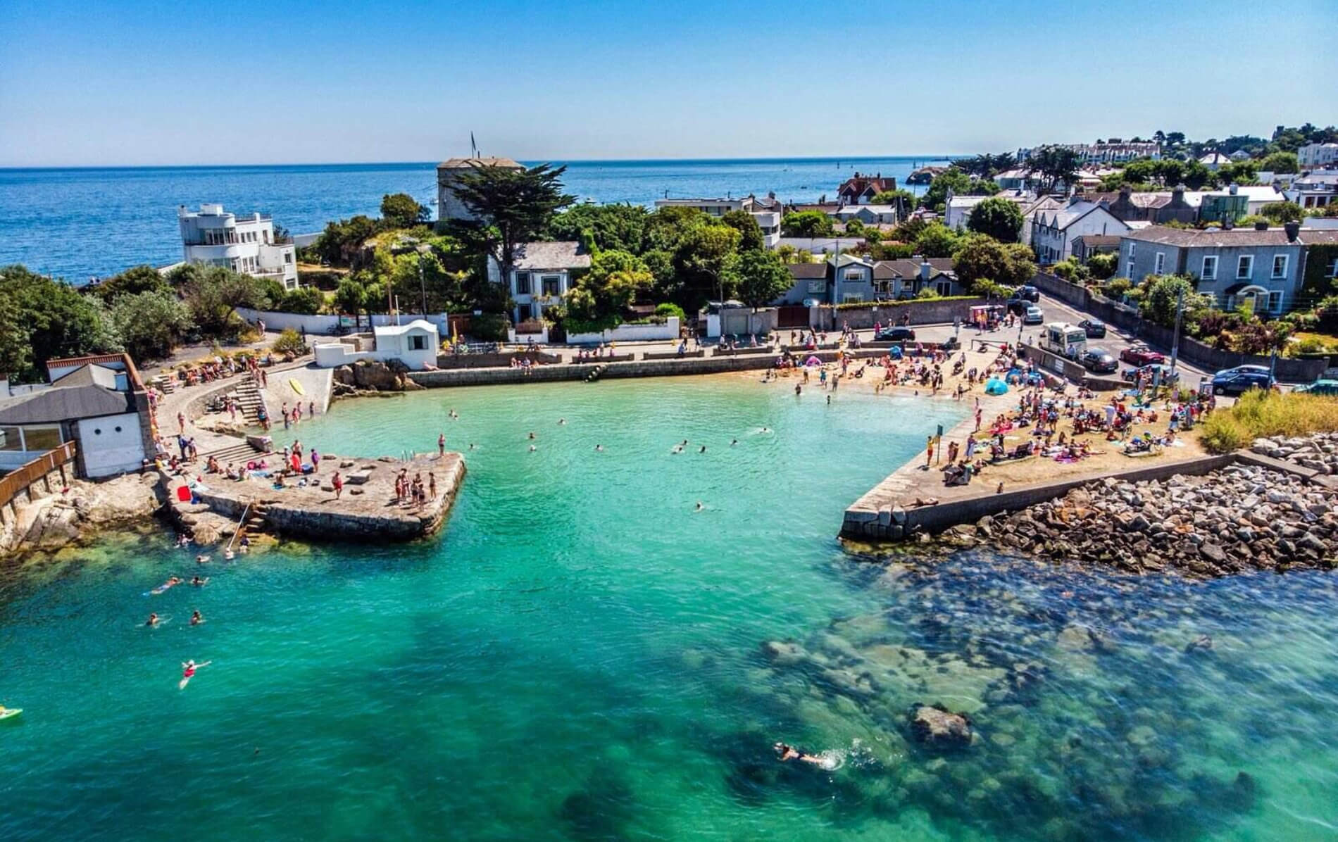 Swimmers and sunbathers enjoy the clear blue water and beach at the Forty Foot bathing spot.
