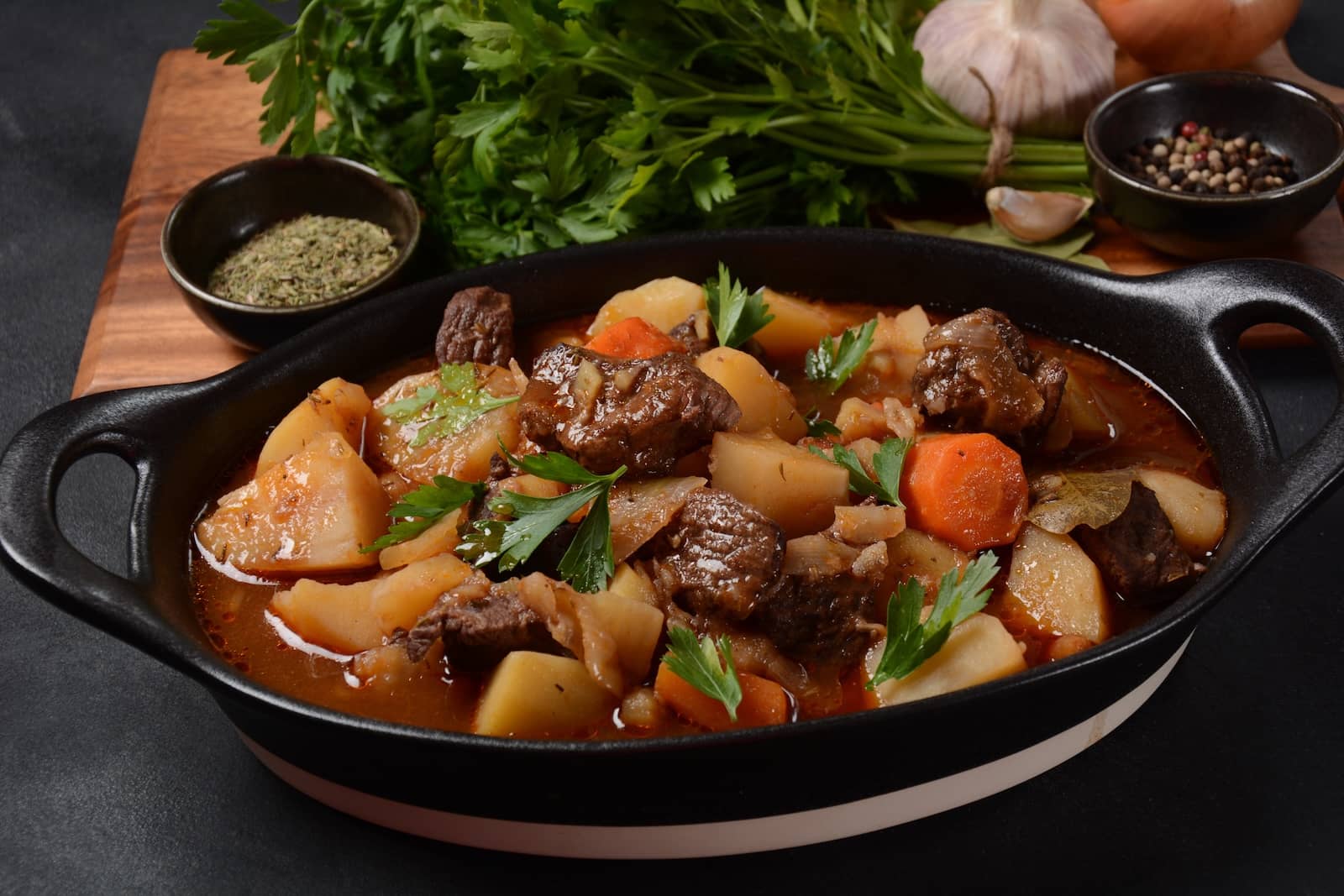 Hearty Irish beef and Guinness stew with potatoes, carrots and fresh parsley in a cast-iron dish.