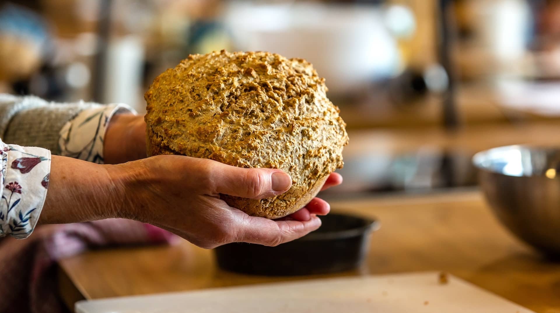 Hands holding a freshly baked loaf of traditional Irish brown bread in a rustic kitchen at Airfield Estate, Dublin.