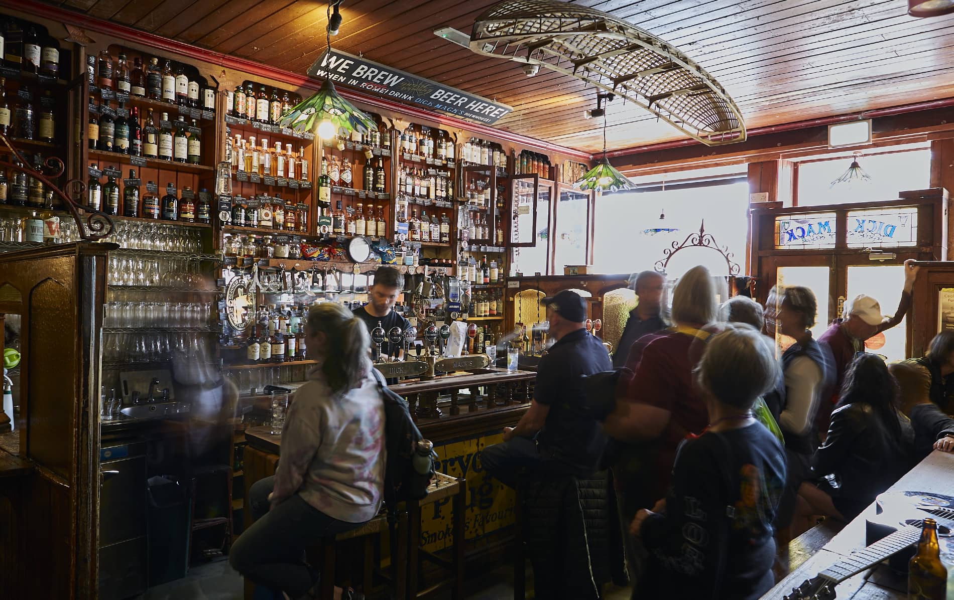 Crowded bar scene inside Dick Mack’s in Dingle, with shelves of whiskey bottles and a lively atmosphere.