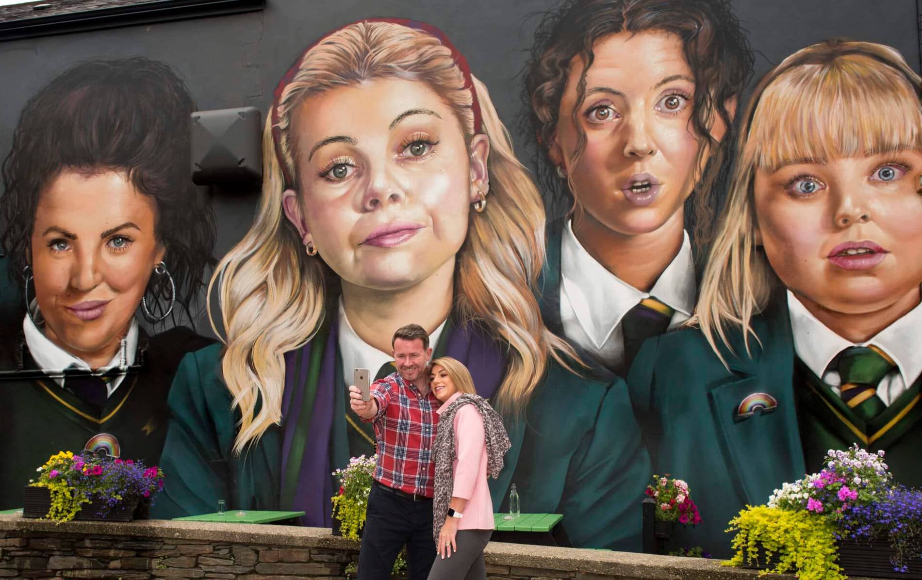 Tourists take a selfie in front of the vibrant Derry Girls mural in Derry~Londonderry, Northern Ireland.