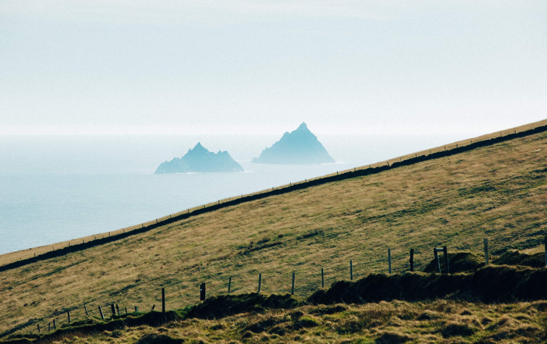 The Skellig Islands rise from the Atlantic, viewed from rolling green hills along the County Kerry coastline.