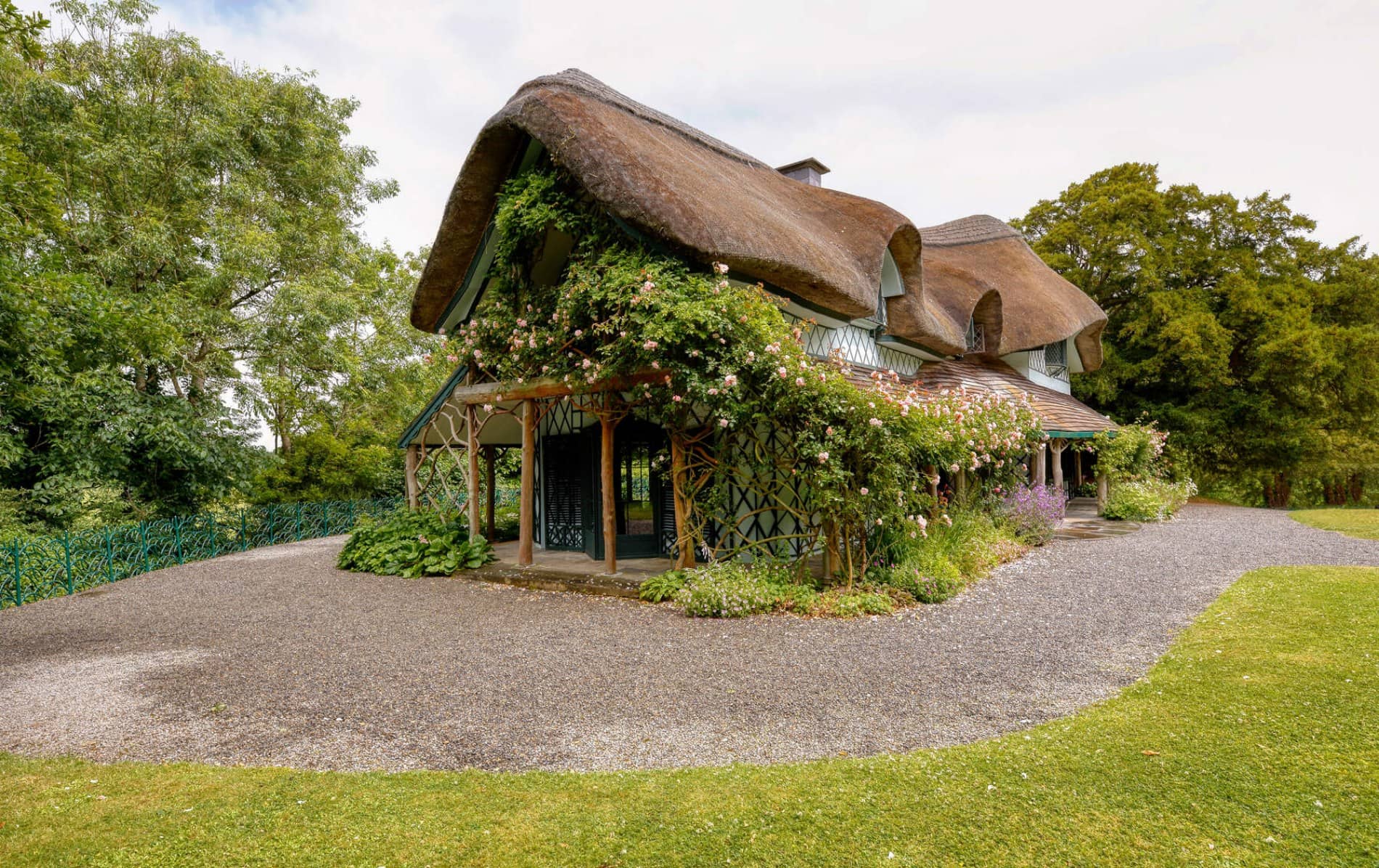 Ornate thatched Swiss Cottage with timber detail, flowers and roses, set in lush gardens in County Tipperary.