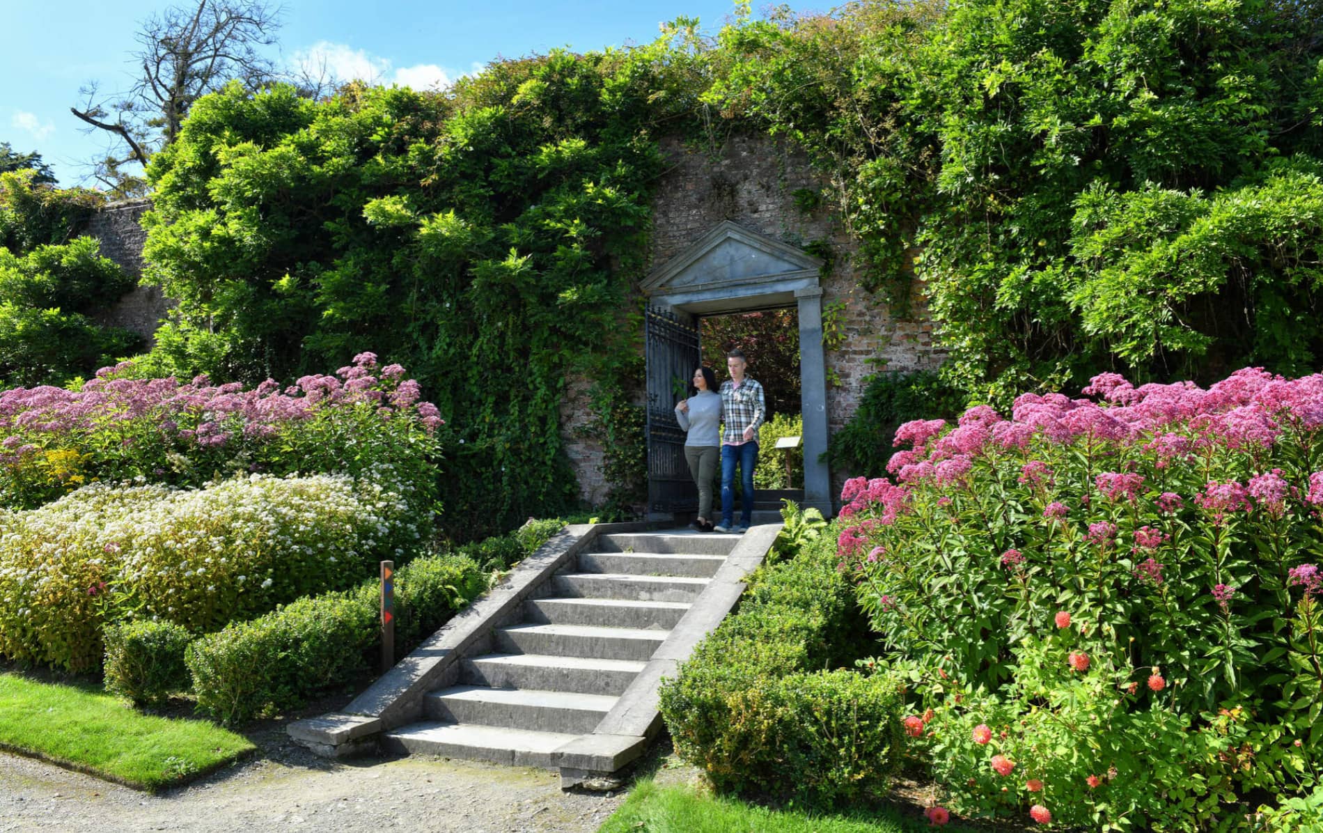 Couple walking through a floral archway in Mount Congreve’s walled garden.