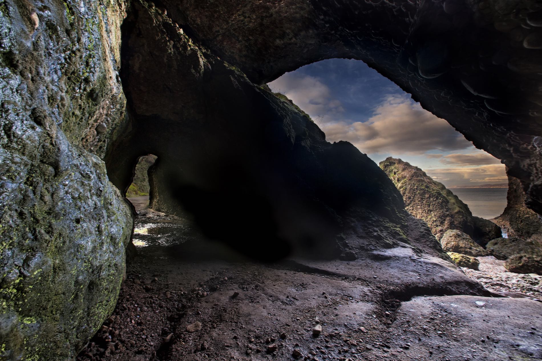 Dark, rocky Cushendun Caves opening to a coastal view under a blue sky in County Antrim, Northern Ireland.