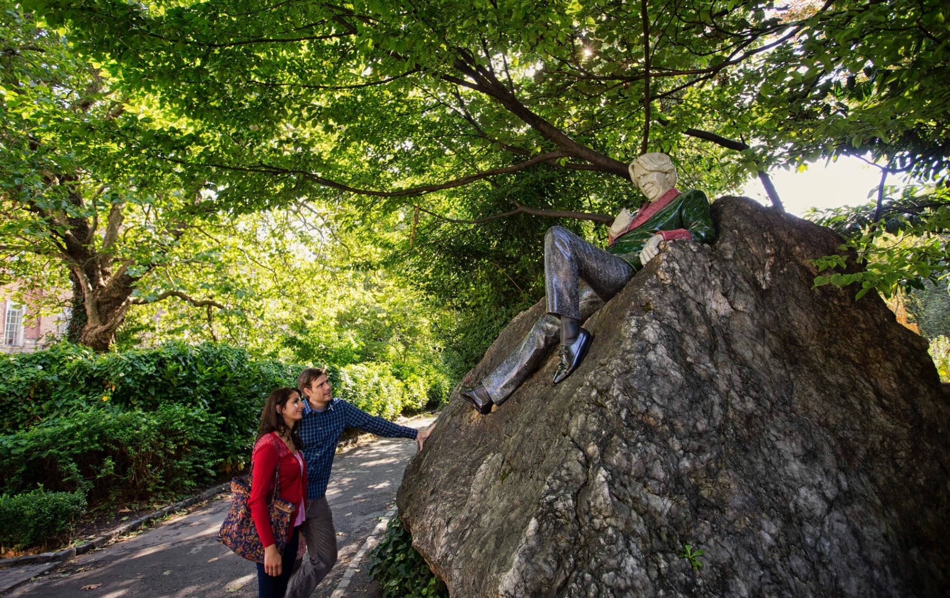 Visitors admire the colourful Oscar Wilde statue lounging on a rock in leafy Merrion Square Park, Dublin.