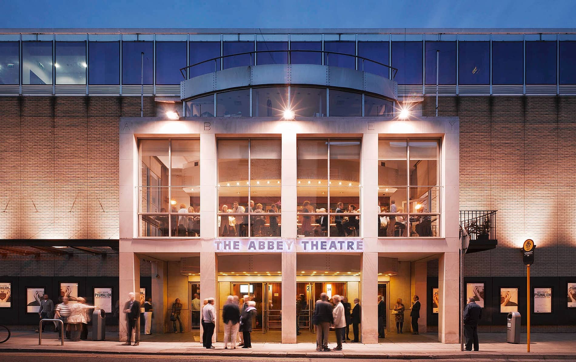 Evening view of Dublin’s Abbey Theatre with warmly lit windows and theatre-goers gathered outside before a show.