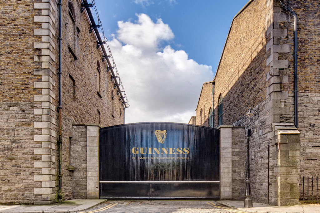 Guinness Storehouse gate at St James’s Gate in Dublin, framed by historic stone buildings and blue skies above.