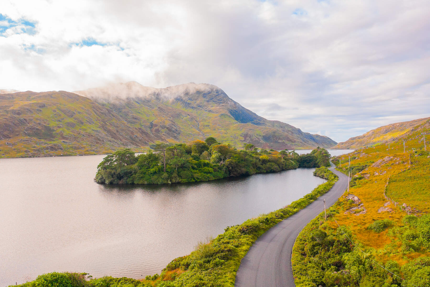 Mountain backdrop with winding road alongside a lake on a cloudy day in Connemara, Ireland.