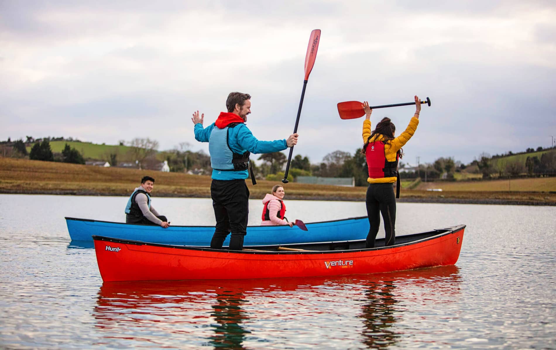 Group canoeing on Strangford Lough in County Down with paddles raised in celebration on calm water.