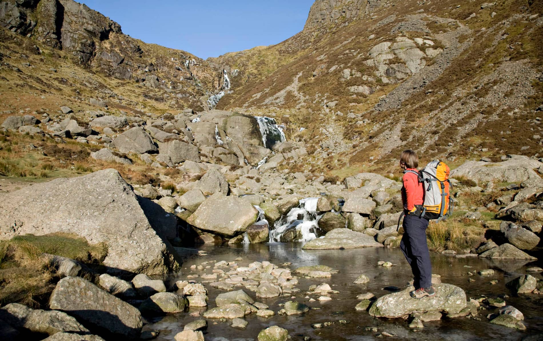 Walker pausing beside boulders near Mahon Falls in the Comeragh Mountains, County Waterford.