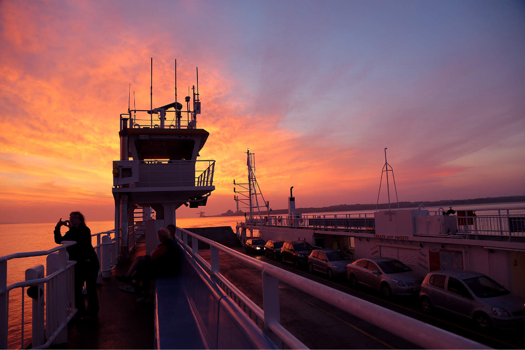 Person photographing sunset from Killimer-Tarbert car ferry in County Clare, with parked cars onboard.