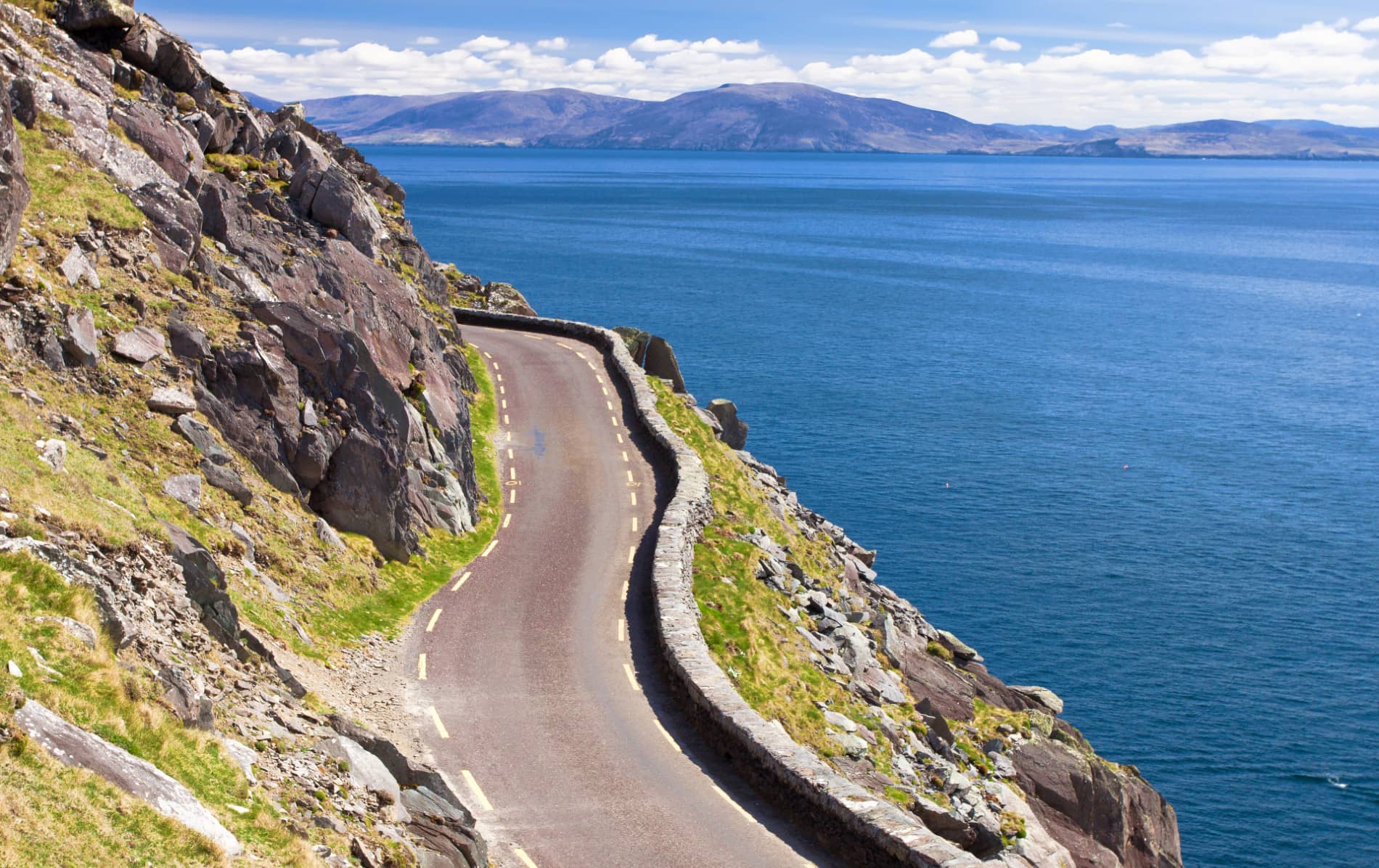 Narrow cliffside road of Slea Head Drive, Kerry, overlooking the Atlantic Ocean and distant mountains.