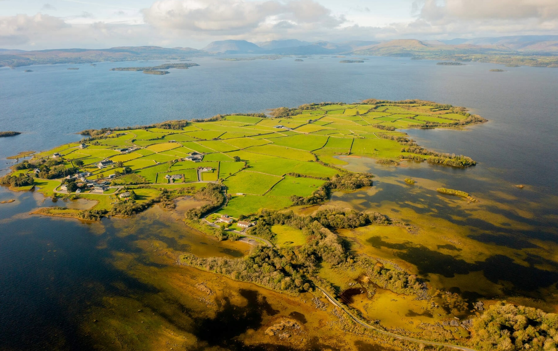 Aerial view of green patchwork fields and scattered cottages beside Lough Corrib in County Galway.