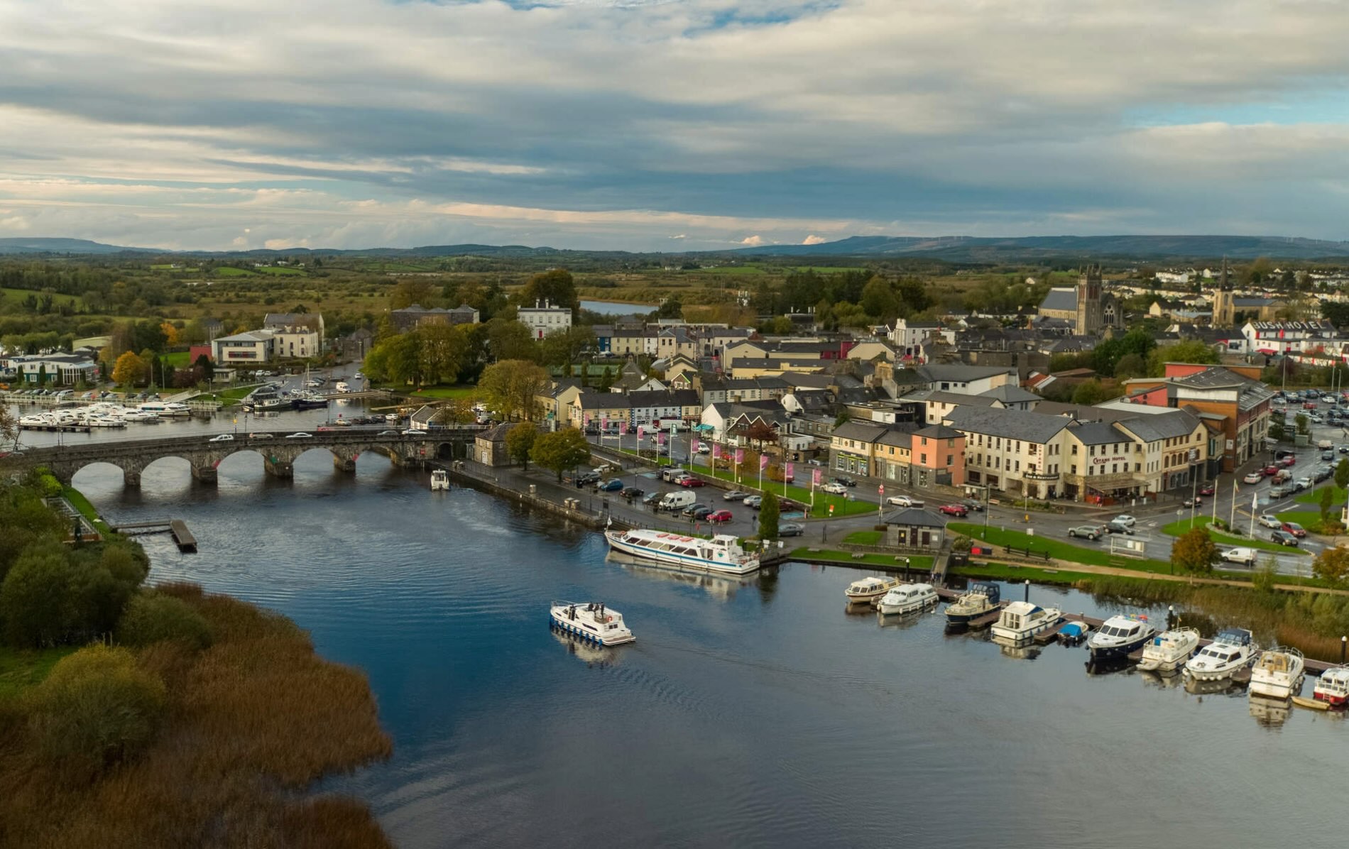 Aerial of Carrick-on-Shannon town, marina and stone bridge crossing River Shannon, surrounded by green fields.