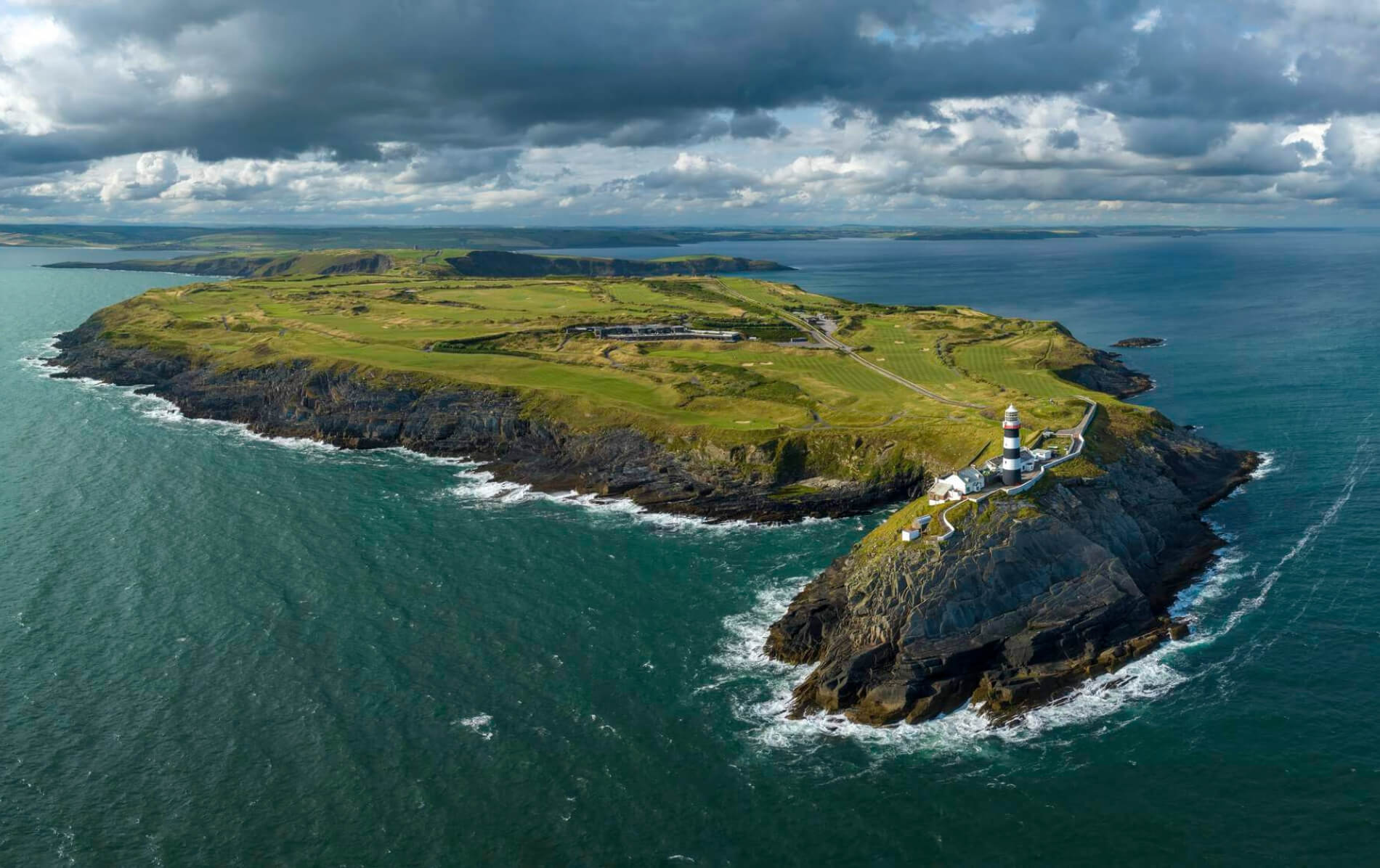 A dramatic aerial view of the Old Head of Kinsale shows a clifftop lighthouse and golf course jutting into the Atlantic.
