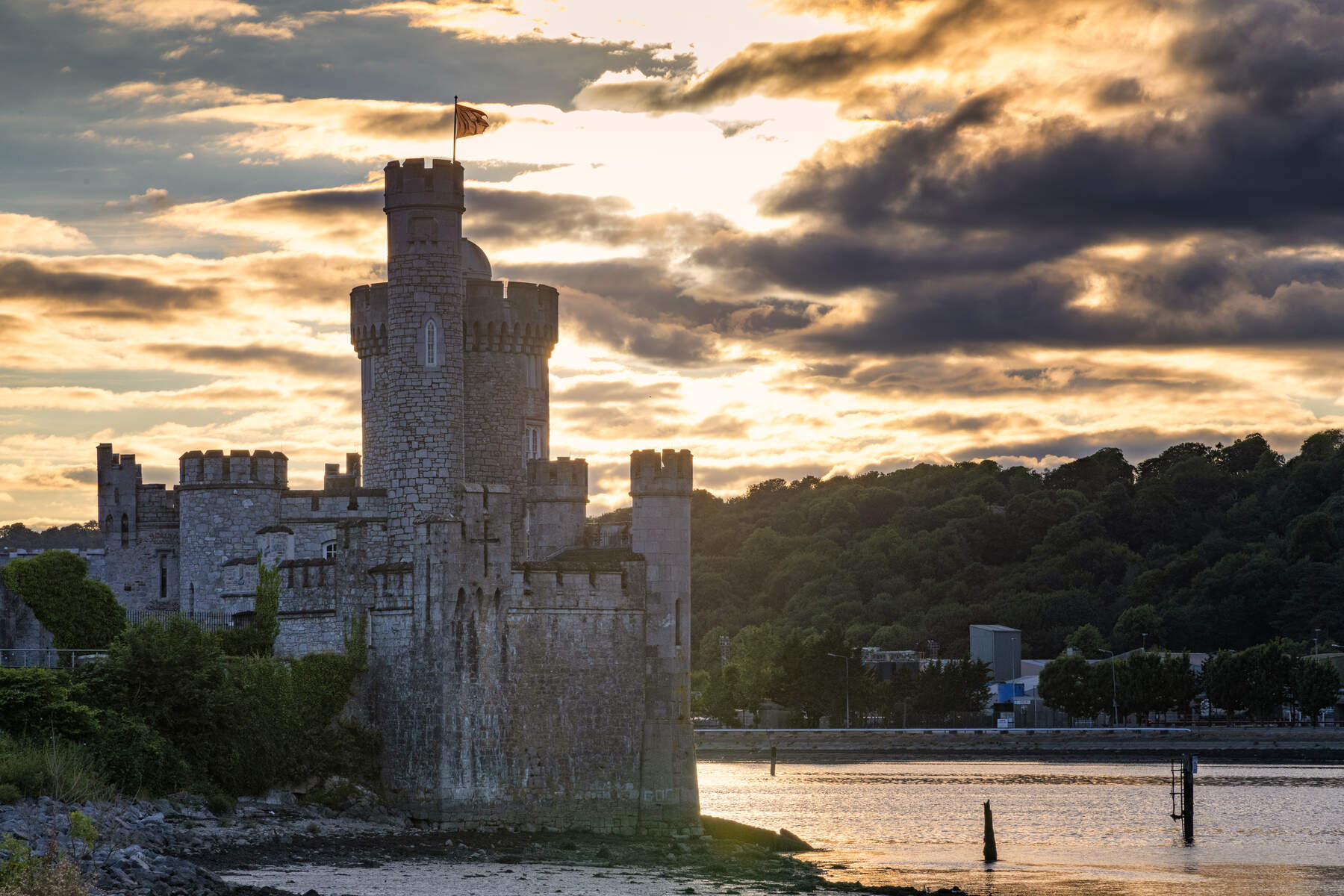 Sunset view of Blackrock Castle on the River Lee, with golden light reflecting off the water and dramatic clouds overhead.