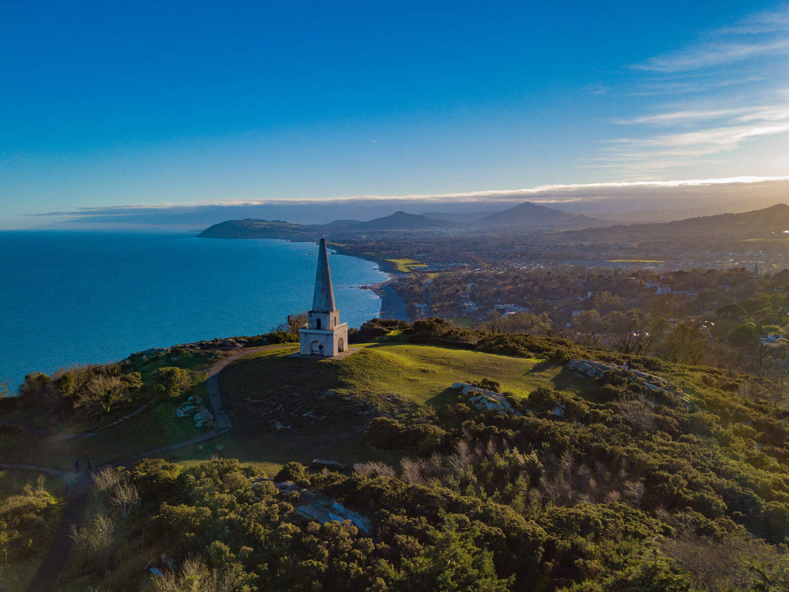 The obelisk atop Killiney Hill overlooks the sweeping coastline and Dublin Bay at sunset.