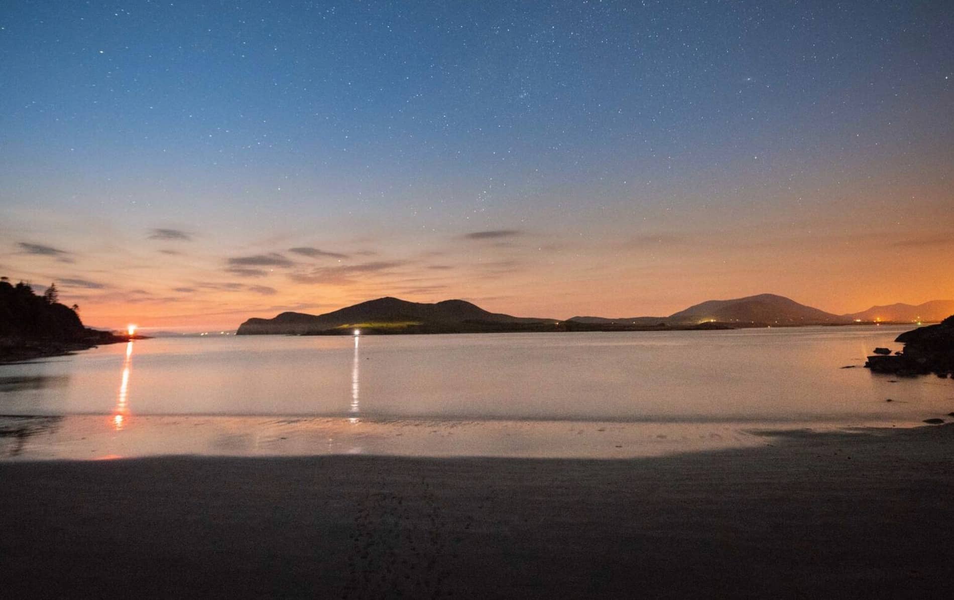A tranquil night view over the Kerry International Dark Sky Reserve, with a star-filled sky reflecting on calm waters.