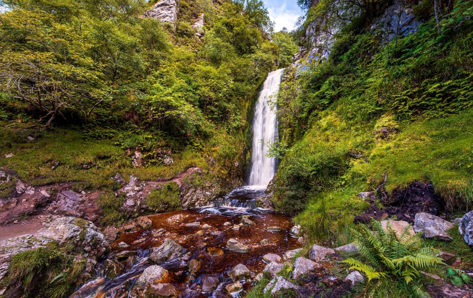 A picturesque waterfall cascades into a rocky pool surrounded by lush green foliage at Glenevin, Donegal.