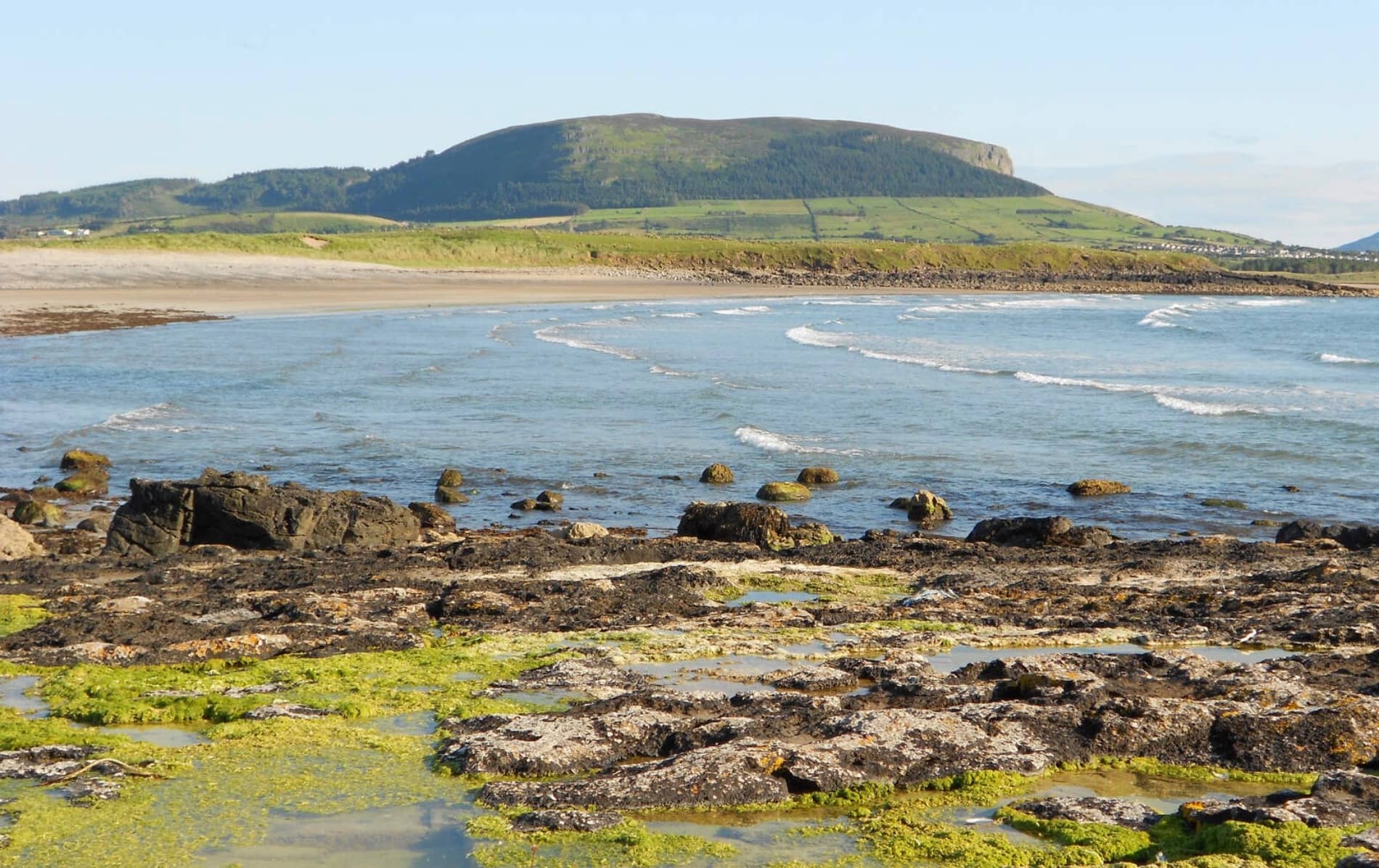 A view of the sea and rocky shore with Queen Maeve’s Cairn, Sligo, visible atop a flat-topped hill in the distance.