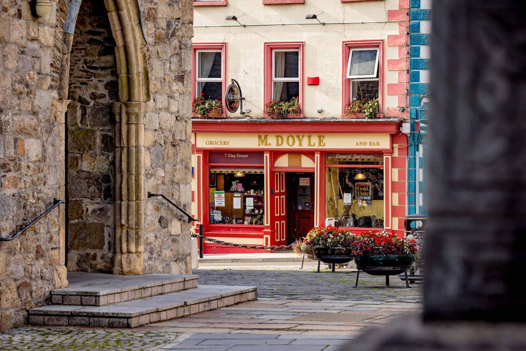 View through a stone archway toward a traditional red-and-cream shopfront in Graiguenamanagh, County Kilkenny.