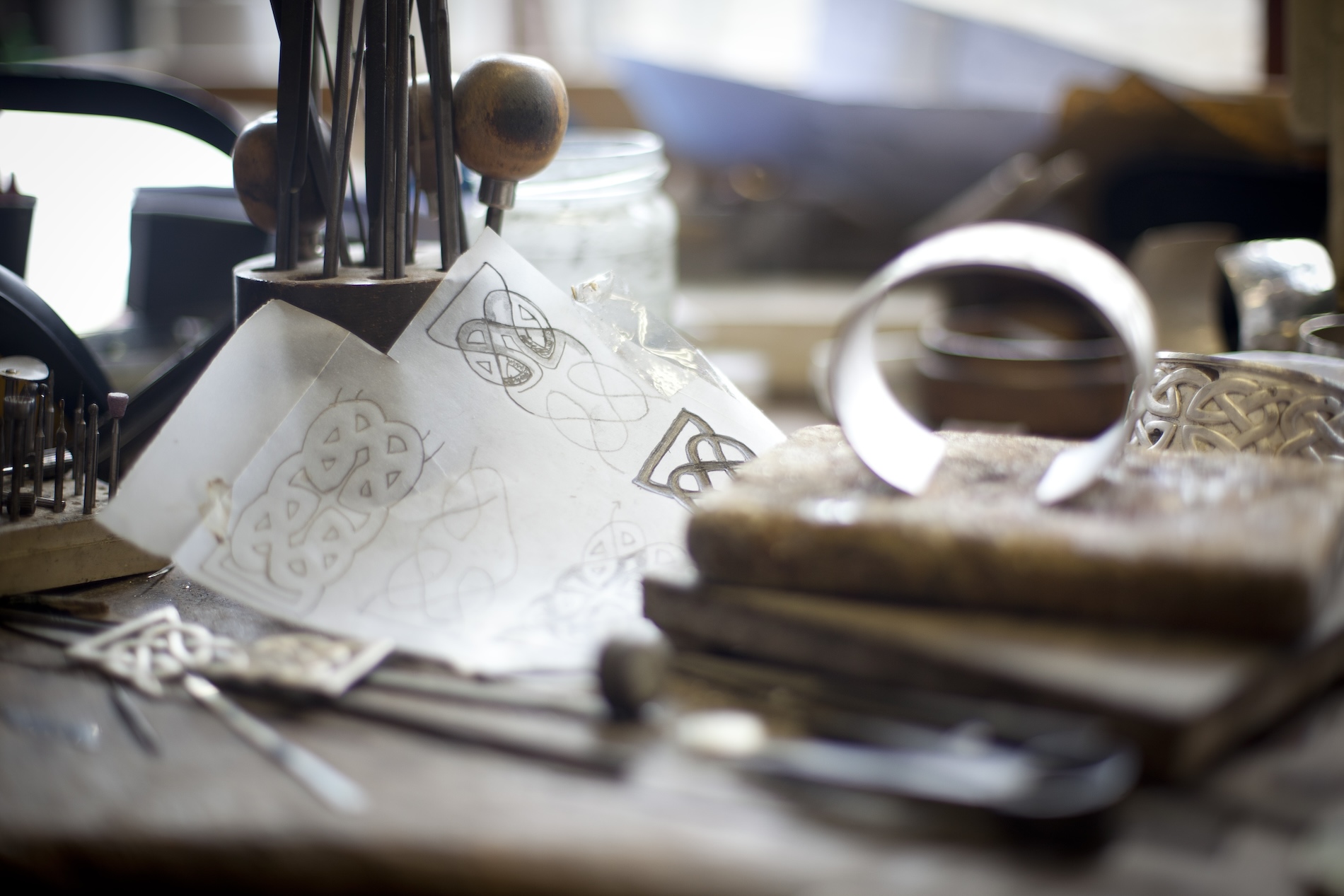 Close-up of sketch papers and metal tools on a wooden workbench at Kilkenny Design Centre.