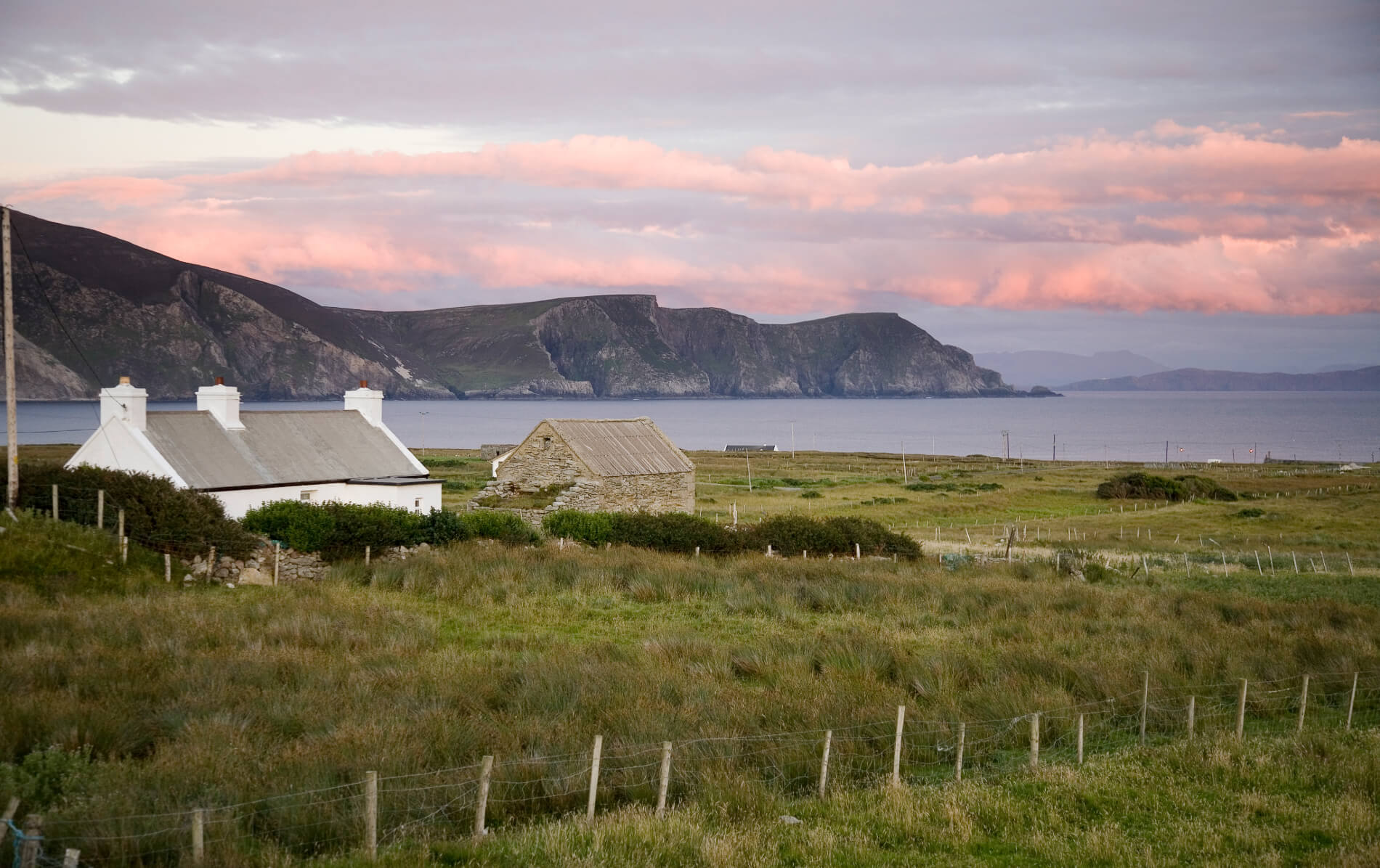 Traditional cottages and stone ruins overlook grassy fields and cliffs above the Atlantic on Achill Island.