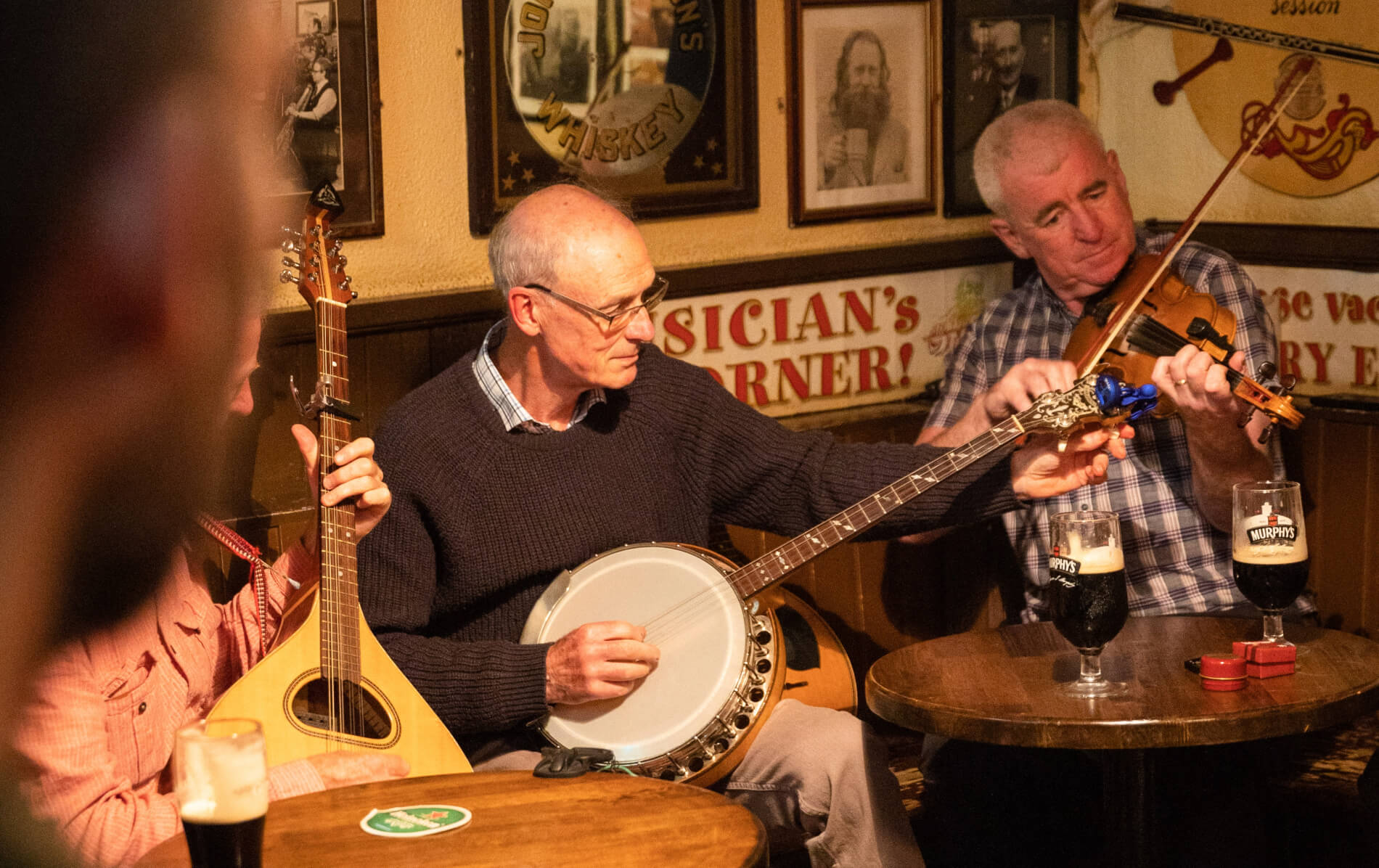 Traditional musicians play banjo and fiddle in a cosy pub with pints of stout on the table.