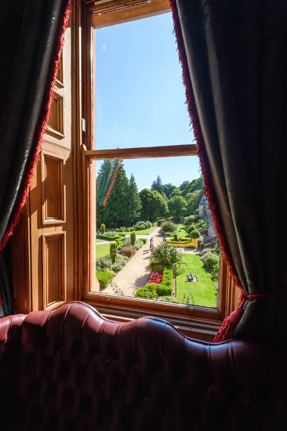 Window view from Belfast Castle interior framing manicured gardens with walking paths and flower beds.