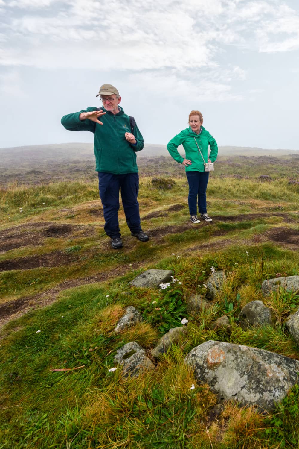 Walking guide explaining Cave Hill history to visitor standing beside grassy ridge.
