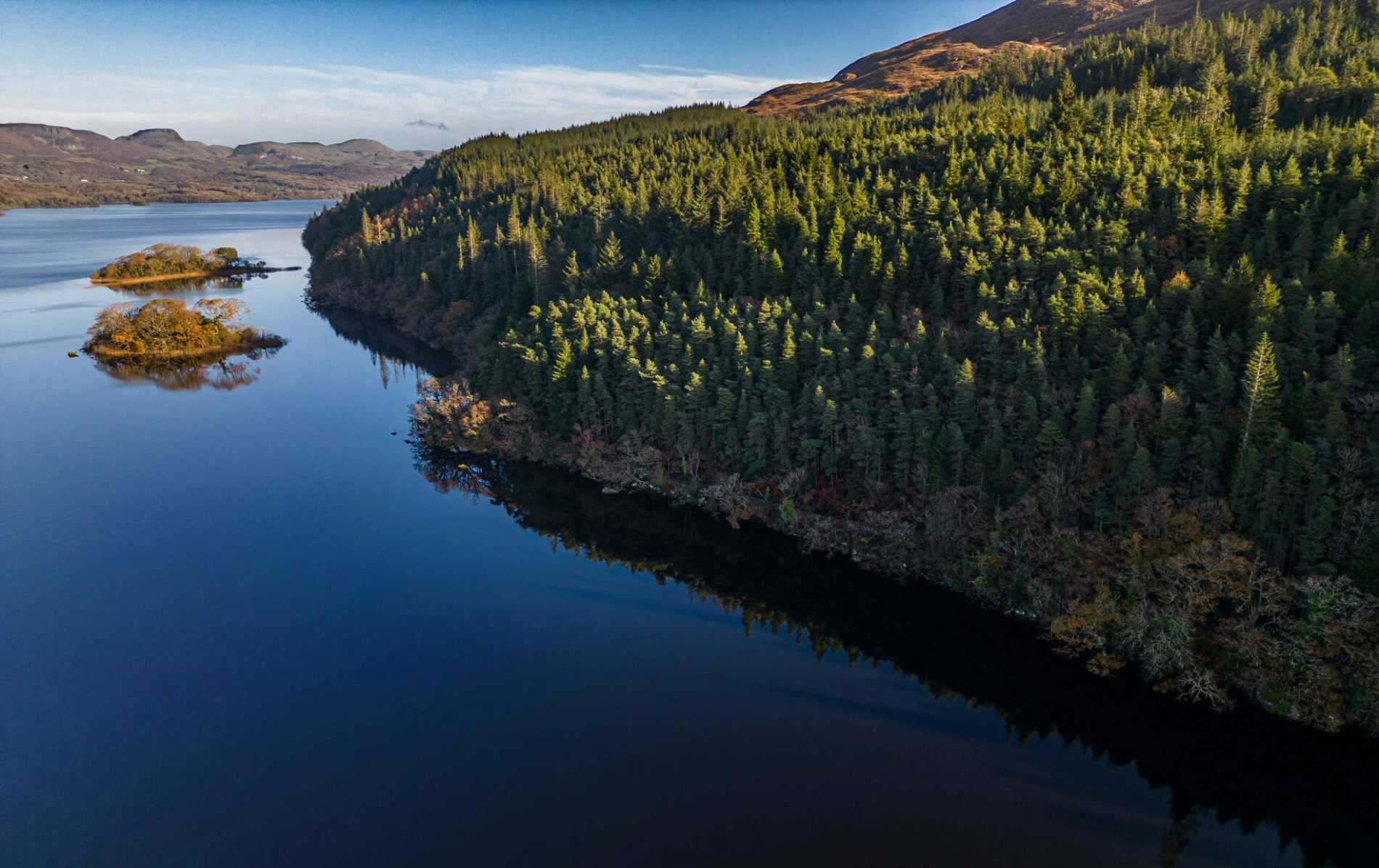 Tranquil Lough Gill in County Sligo with wooded islands and dense forest shoreline reflecting on calm water.