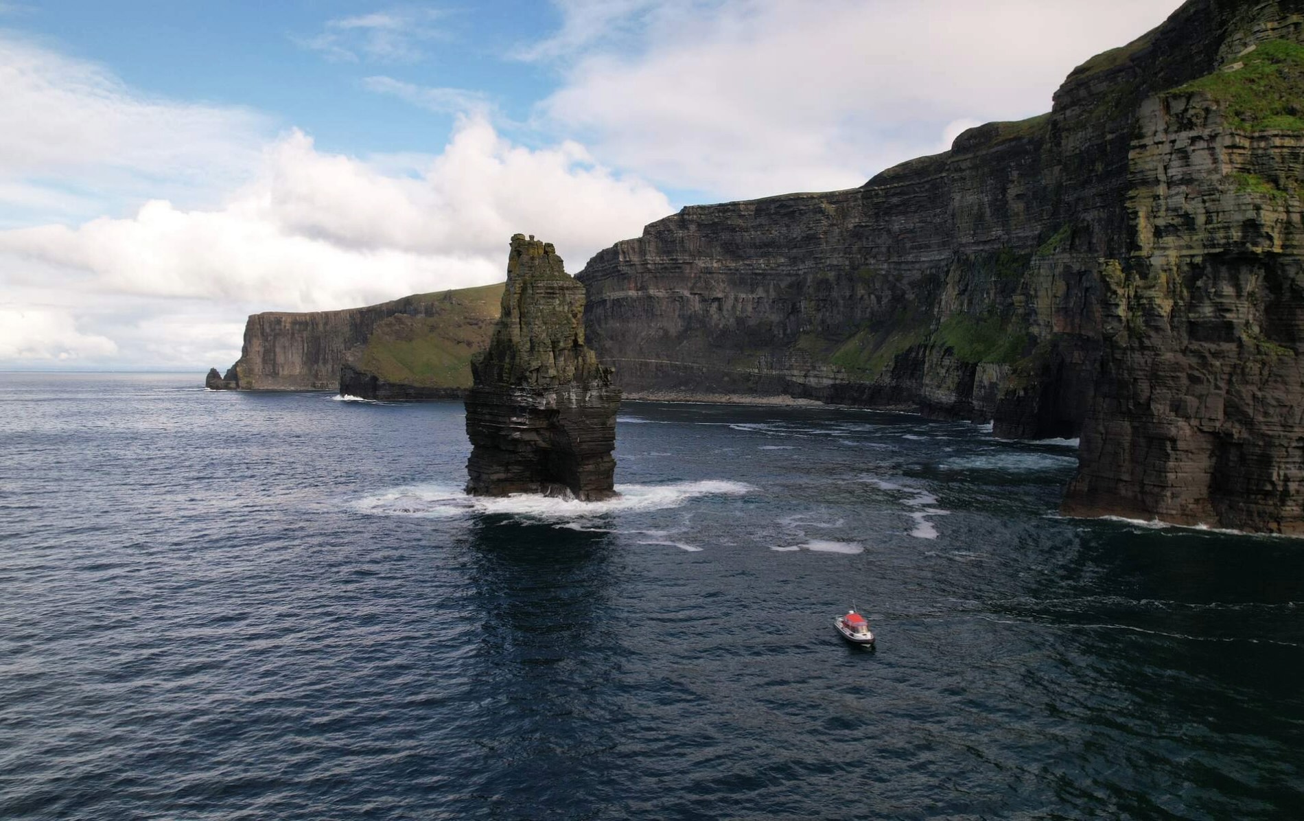 Boat sailing near the Cliffs of Moher in County Clare with sea stack Branaunmore rising dramatically from Atlantic waves.