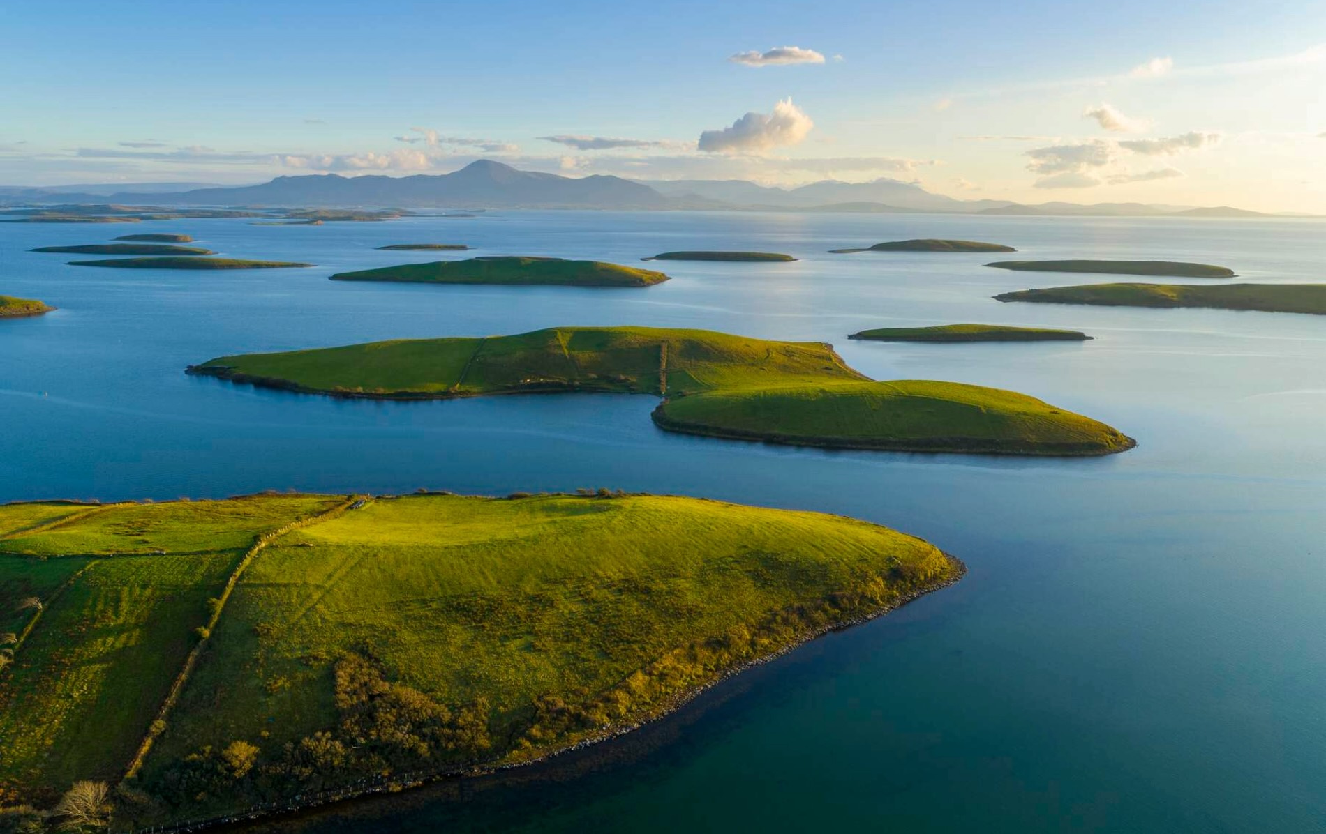 Aerial view of Clew Bay in County Mayo with green drumlin islands dotting the blue ocean and Croagh Patrick in distance.
