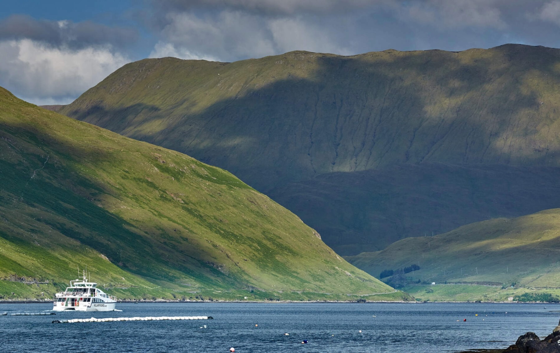 Passenger boat cruising Killary Harbour fjord in County Galway surrounded by steep green mountains.