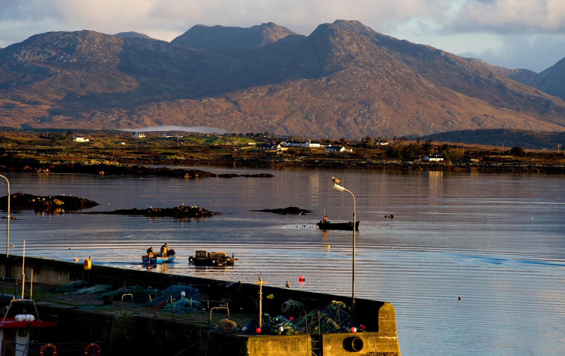 Roundstone Harbour in Galway with fishing boats and nets, set against Twelve Bens mountain range in evening light.