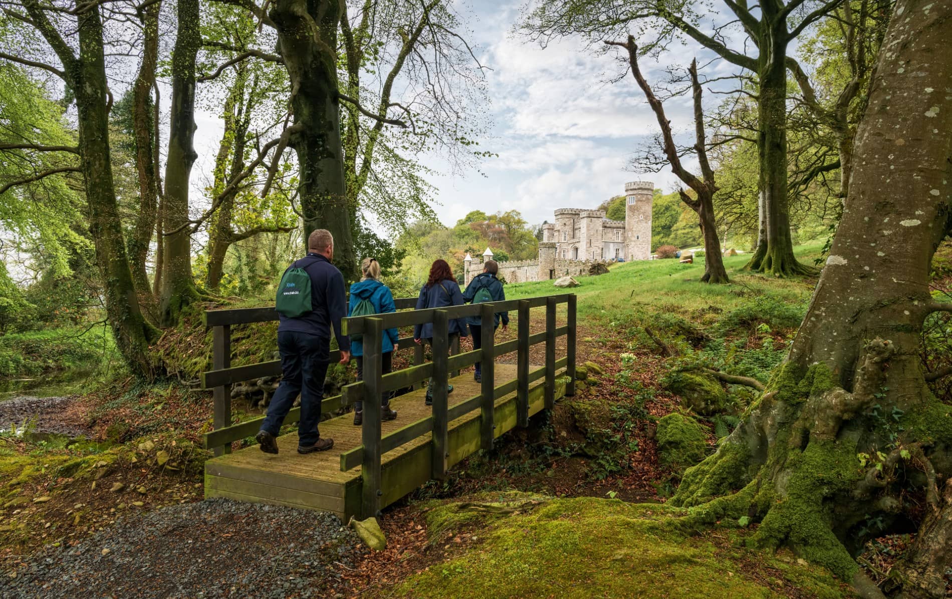 Group of walkers crossing wooden bridge in forest towards stone Killeavy Castle in County Armagh.